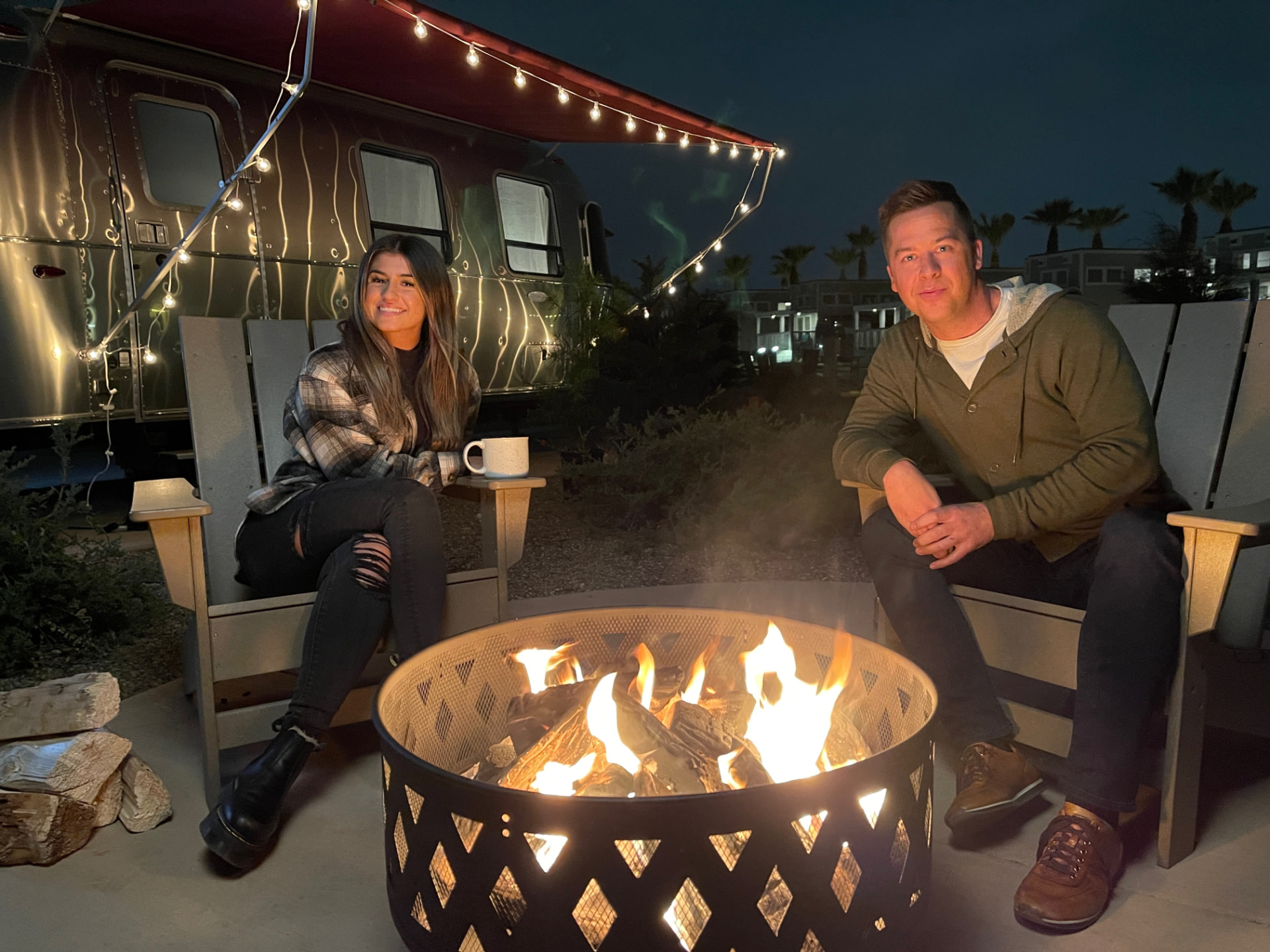 Host and guest talking in chairs around a fire pit at night